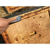 Hand using a metal beekeeping tool with an angled edge to scrape wax and debris from a wooden hive frame, featured in Farm, Garden & Tool and Beekeeping Supplies collections.