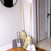 Two traditional brooms with wooden handles standing next to two sturdy metal dustpans with hanging loops, displayed in a home entryway, highlighting household cleaning utensils in USA Made and Best Sellers collections.