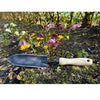 Handcrafted forged transplant trowel with a narrow black blade and smooth wooden handle resting on soil among blooming garden flowers, ideal for Farm, Garden & Tool and Digging and Cultivating collections.