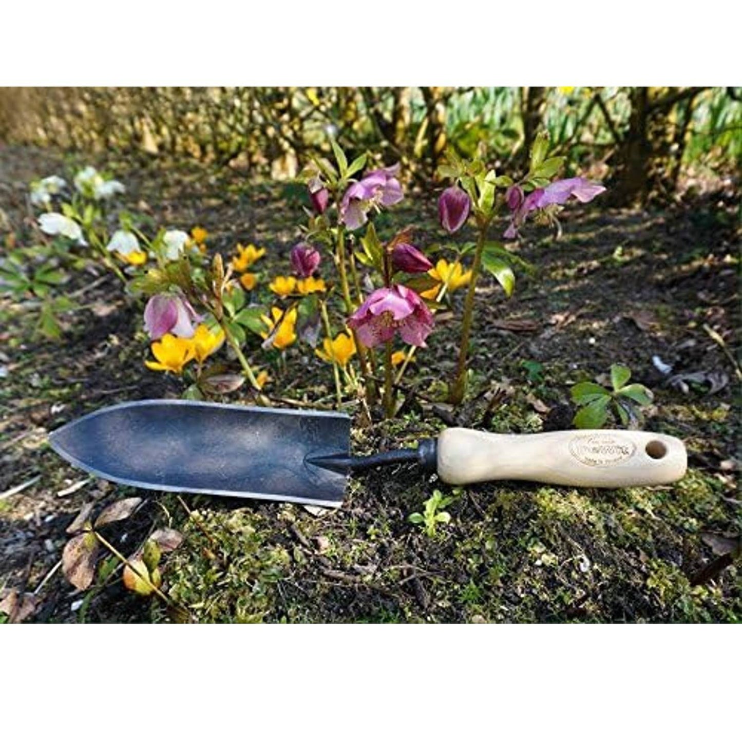 Handcrafted forged transplant trowel with a narrow black blade and smooth wooden handle resting on soil among blooming garden flowers, ideal for Farm, Garden & Tool and Digging and Cultivating collections.