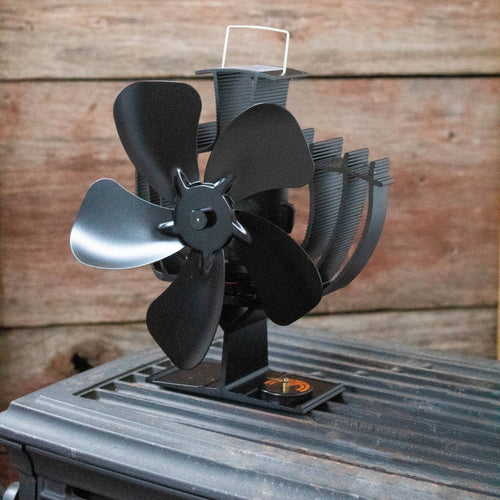 Black heat-powered stove fan with four curved blades and finned heat sink base that oscillates to distribute warm air efficiently, featured in stoves and hearth accessories collections.