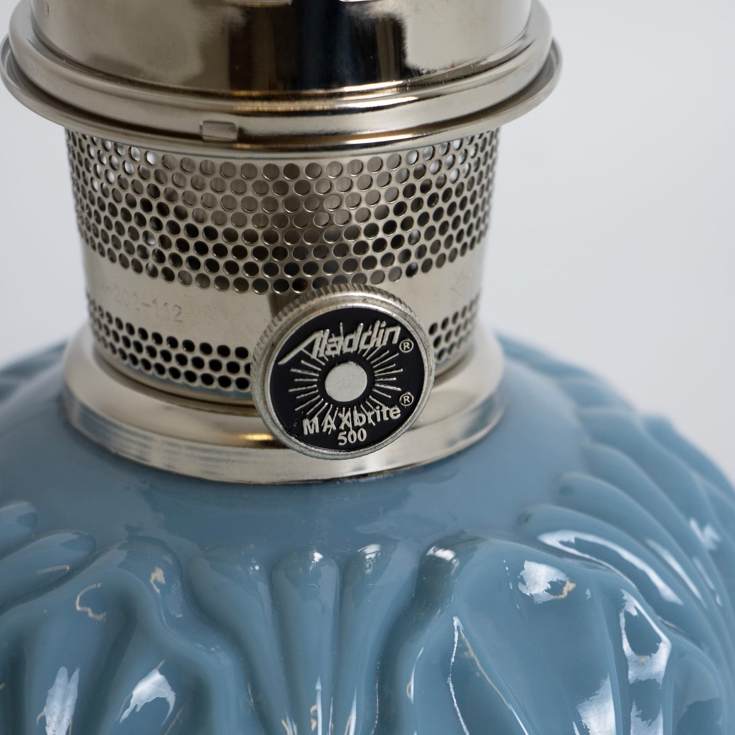 Close-up of a handcrafted Aladdin burner with perforated metal body and control knob on a glossy blue glass base, ideal for Lamps & Lighting, Oil Lamps, Table Lamps, Best Sellers, and Promo Eligible collections.