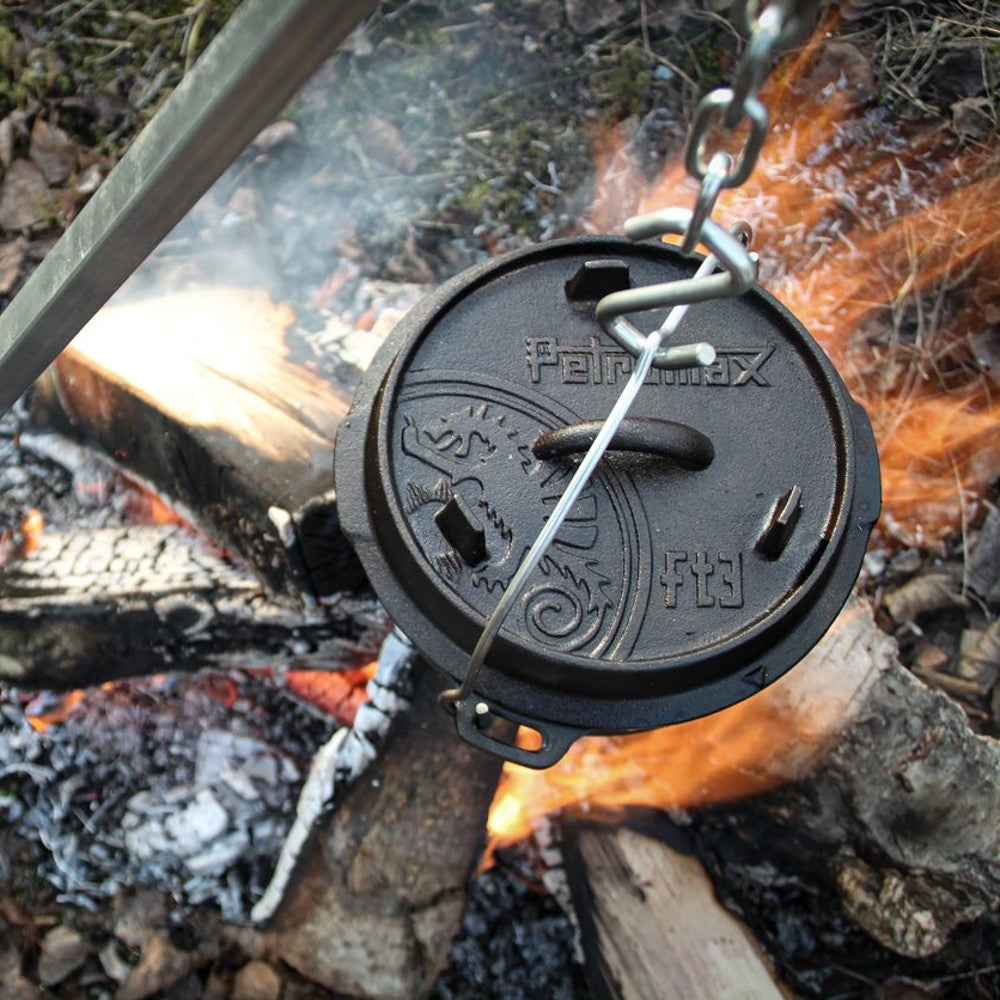 Cast iron Dutch oven with legs suspended over an open campfire, featuring an embossed lid with vent holes, perfect for outdoor cooking in Kitchen & Food, Cookware, Cast Iron, Best Sellers, and Promo Eligible collections.