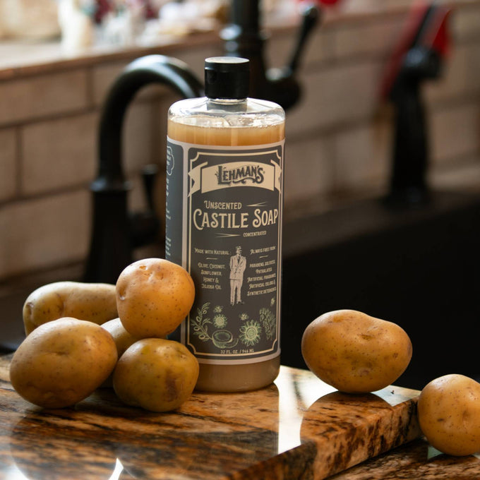 Clear bottle of Lehman's handcrafted unscented Castile liquid soap surrounded by fresh potatoes on a kitchen counter, highlighting multi-use, natural, USA made soap for health, grooming, and soapmaking collections.