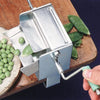 Metal pea sheller with a green crank handle clamped to a wooden table, shelling fresh peas onto a plate, crafted in USA for Kitchen & Food, Specialty Equipment, and Peelers and Pitters collections.