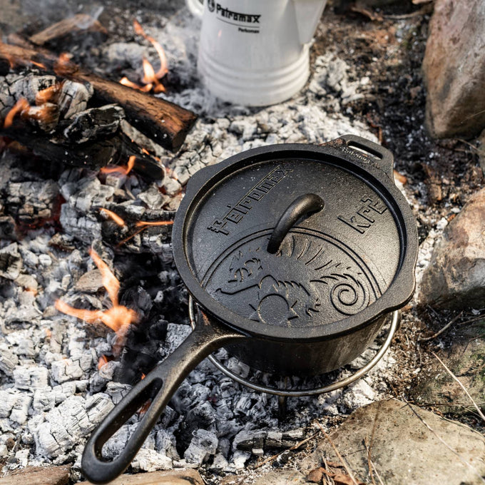 Handcrafted cast iron saucepan with embossed lid featuring a lizard design, cooking over hot embers, perfect for farm, garden, camping, kitchen, cookware, and cast iron collections.