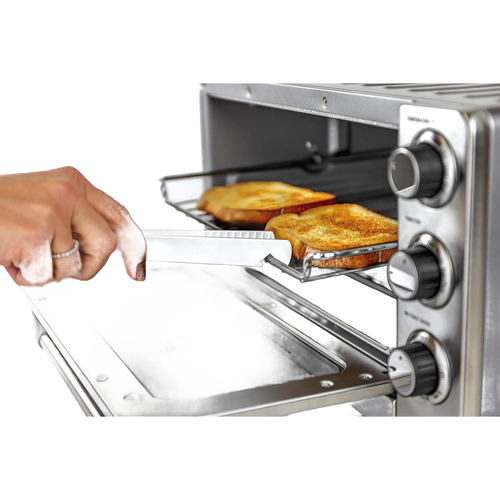 Hand holding white butterie toaster tongs with serrated teeth removing toasted bread from a stainless steel toaster oven, featured in Kitchen & Food and Kitchen Gadgets collections.