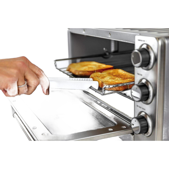 Hand holding white butterie toaster tongs with serrated teeth removing toasted bread from a stainless steel toaster oven, featured in Kitchen & Food and Kitchen Gadgets collections.
