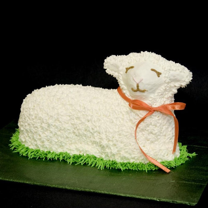 Handcrafted Easter lamb-shaped cake decorated with white frosting and an orange ribbon, styled on green icing grass, featured in Kitchen & Food, Cookware, Baking Supplies, USA Made, Best Sellers, Promo Eligible collections.