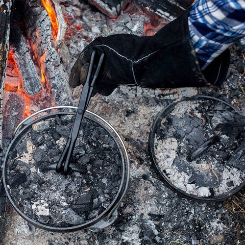 Black leather glove with deep cuff protects hand while handling hot cast iron cookware over glowing campfire coals, featured in Camping, Kitchen & Food, and Best Sellers collections.