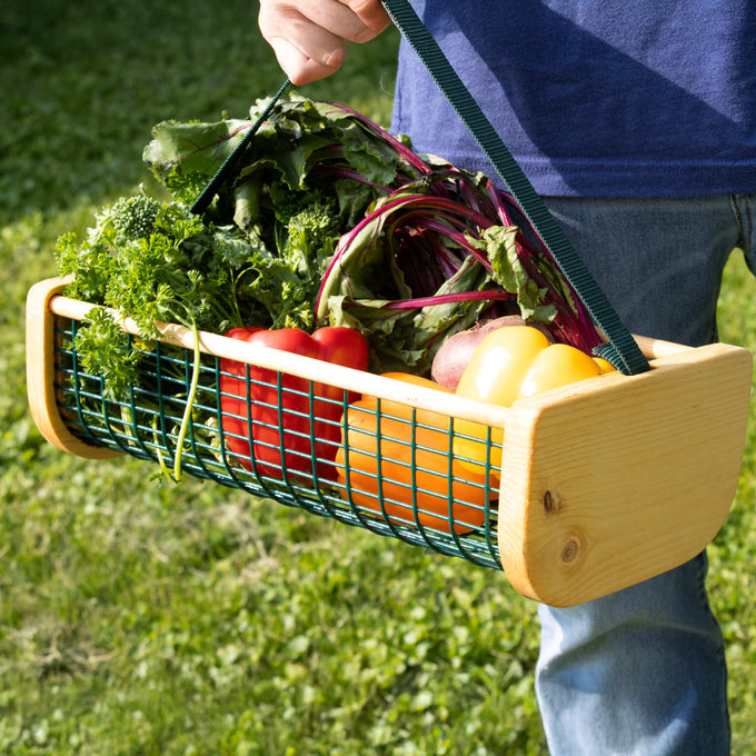 Harvest basket with wooden ends and green wire mesh sides, filled with fresh vegetables and greens, held by a person outdoors, part of Farm, Garden & Tool and USA Made collections.