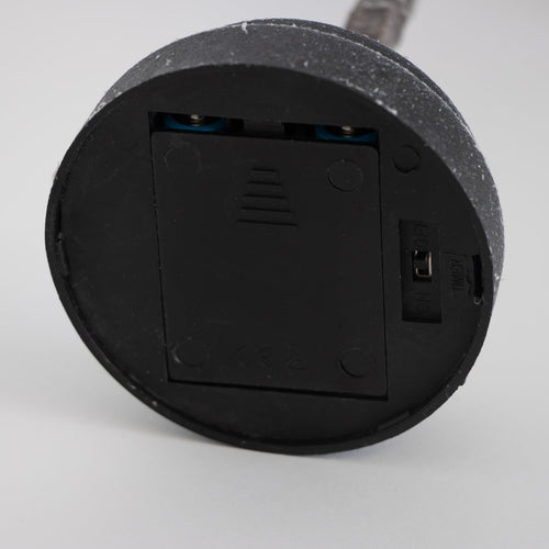 Bottom view of a black round battery compartment with a sliding cover and an on/off switch, part of a handcrafted decorative holiday item from Home & Decor, Holiday Decor, Best Sellers, and Promo Eligible collections.