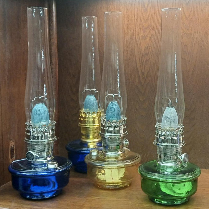 Set of four handcrafted oil lamps with colored glass bases in blue, amber, and green, featuring gleaming brass or nickel burners, ideal for Farm, Garden & Tool and Lamps & Lighting collections.