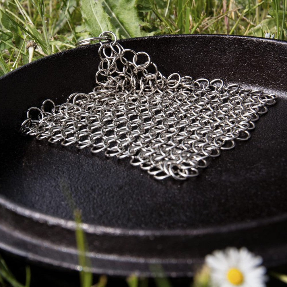 Stainless steel chainmail cleaner placed inside a cast iron skillet outdoors on grass, handcrafted for scrubbing cast and wrought iron cookware, featured in Home & Decor and Household Cleaning collections.