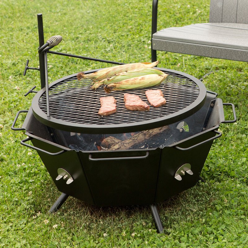 Heavy-duty steel outdoor grill and fire pit in use on grass, with corn and meat cooking on the adjustable grill grate, ideal for camping and backyard grilling in USA Made and Farm, Garden & Tool collections.