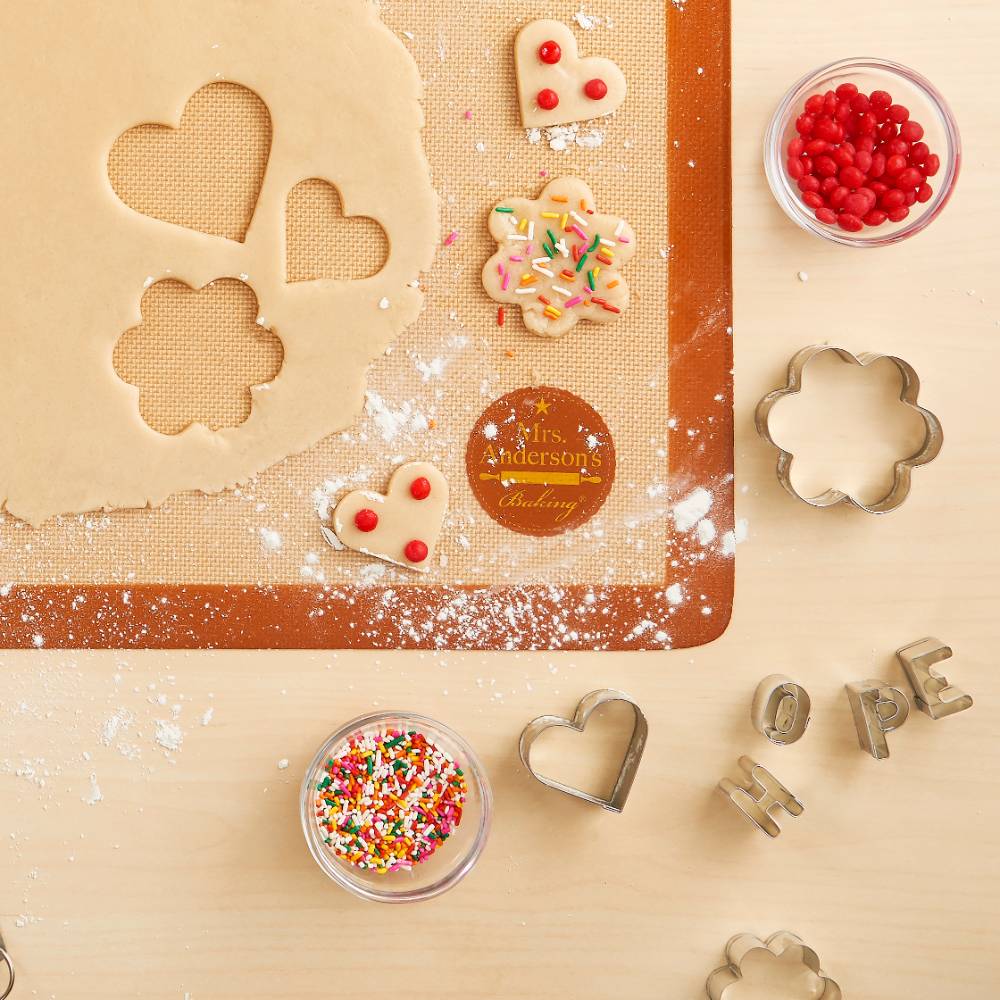 Silicone baking mat with dough cut into heart and flower shapes, decorated cookies with sprinkles and red candy, metal cookie cutters, and bowls of colorful sprinkles in Kitchen & Food, Cookware, Baking Supplies, Best Sellers, Promo Eligible collections.