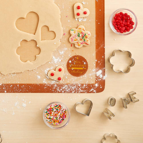 Silicone baking mat with dough cut into heart and flower shapes, decorated cookies with sprinkles and red candy, metal cookie cutters, and bowls of colorful sprinkles in Kitchen & Food, Cookware, Baking Supplies, Best Sellers, Promo Eligible collections.