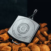 Square cast iron grill pan with raised handle, showcasing handcrafted USA-made Blacklock branding, resting on natural rustic wood pieces, ideal for Kitchen & Food and Cookware collections.