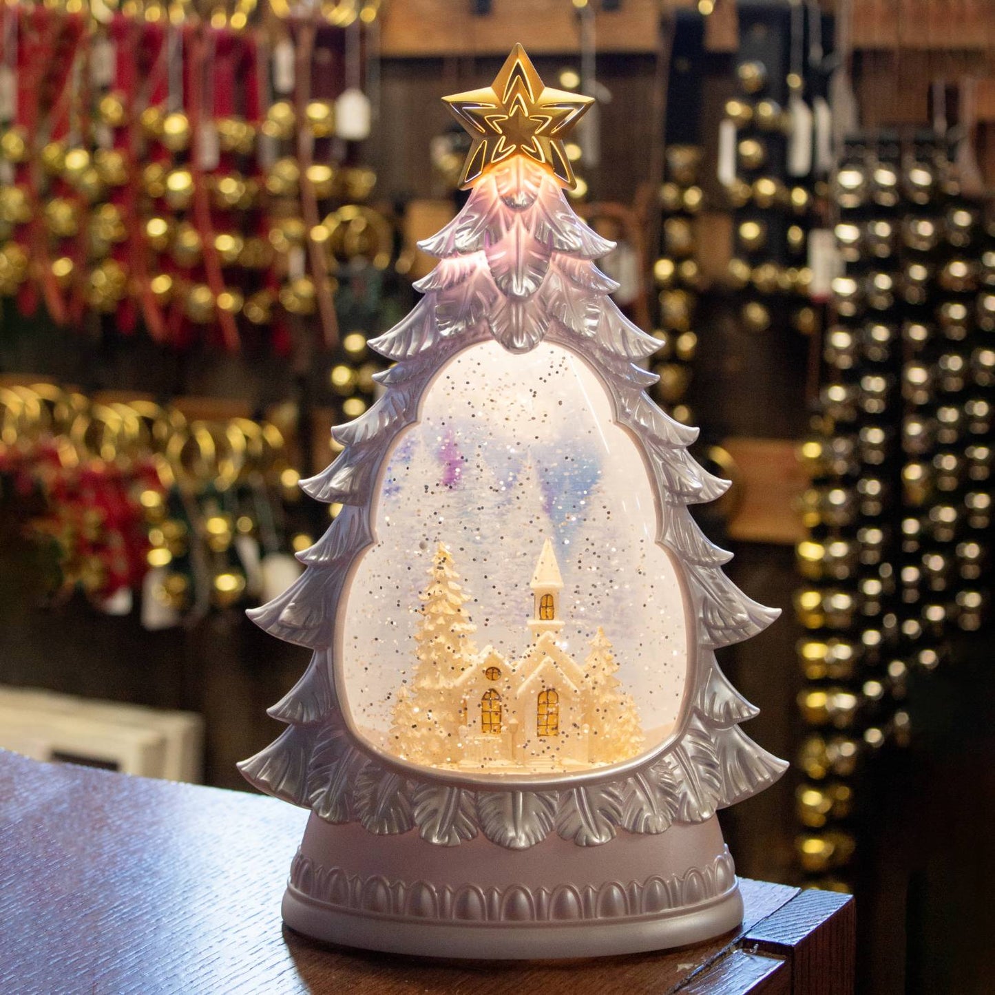 Illuminated shimmering water globe shaped like a Christmas tree with a snowy church scene inside, featuring a 6-hour timer, perfect for home and holiday decor collections.