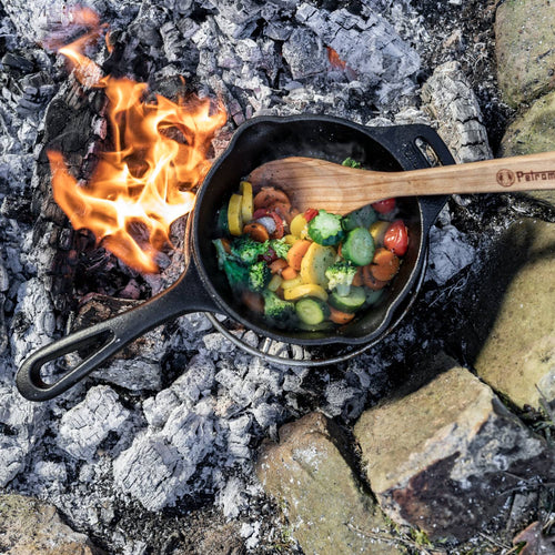 Handcrafted cast iron saucepan with long handle cooking colorful mixed vegetables over open fire, ideal for camping, farm, garden, kitchen, cookware, and cast iron collections.