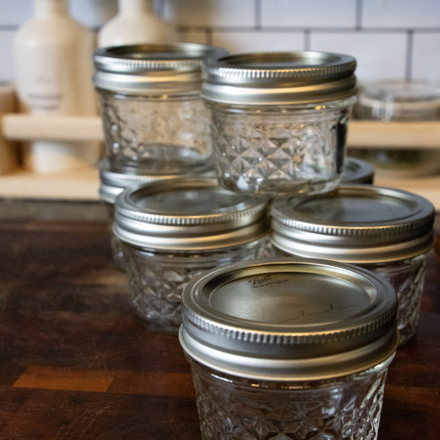 Group of clear glass quilted regular-mouth jelly jars with silver metal lids on wooden surface, designed for canning and food preservation, part of USA Made and Kitchen & Food collections.