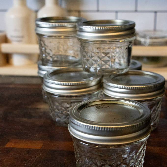Group of clear glass quilted regular-mouth jelly jars with silver metal lids on wooden surface, designed for canning and food preservation, part of USA Made and Kitchen & Food collections.