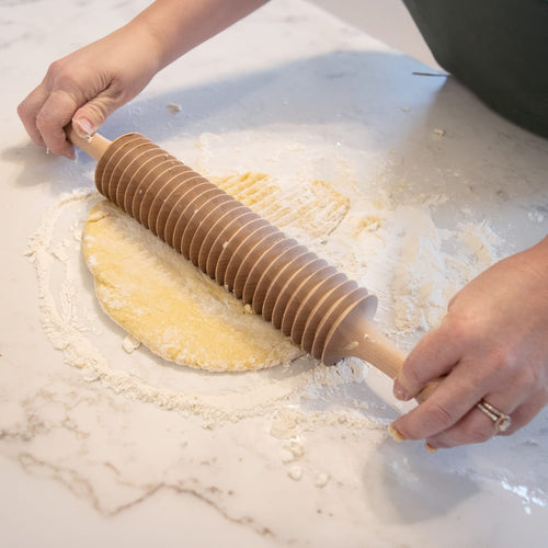 Hands using a handcrafted unfinished cherry wood noodle cutter to slice dough on a floured marble surface, highlighting Kitchen & Food, Food Prep, and Amish Made collections.