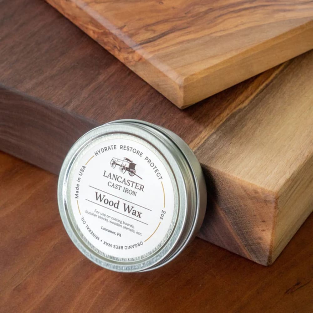 Small metal tin of Lancaster Wood Wax Conditioner made with organic beeswax and food-grade mineral oil, displayed next to smooth wooden cutting boards for Kitchen & Food and Food Prep collections.