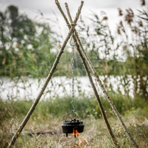 Sturdy outdoor tripod made from natural branches held by a stainless steel lashing set with hooks and chain, supporting a cooking pot over an open campfire in a grassy camping area, ideal for Farm, Garden & Tool, Camping, Best Sellers, and Promo Eligible collections.