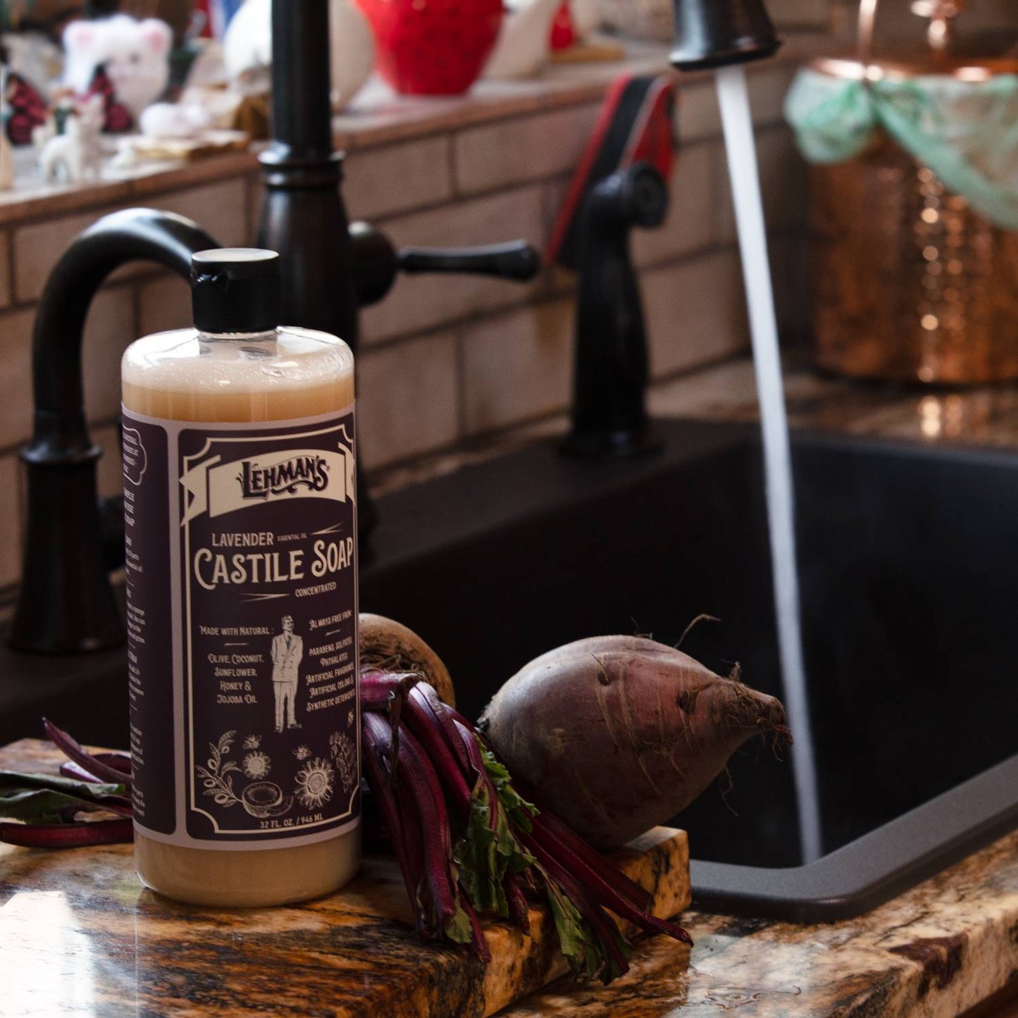Amber bottle of Lehman's Lavender Castile soap near fresh root vegetables on a kitchen counter next to a running faucet, highlighting handcrafted, multi-use, USA made soap for Health & Wellness and Grooming collections.