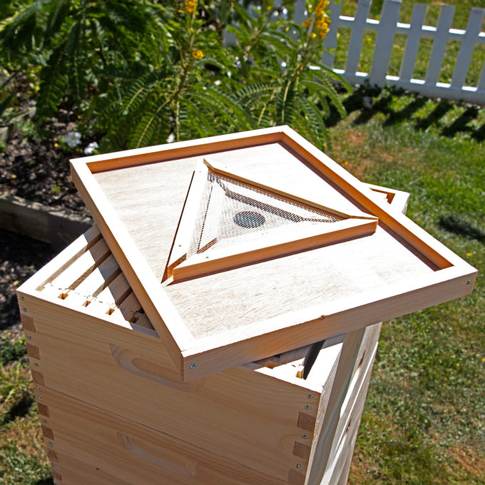 Handcrafted Amish-made triangle bee escape board with a mesh maze design resting on a wooden 10-frame beehive outdoors, ideal for chemical-free beekeeping in farm and garden tools collections.