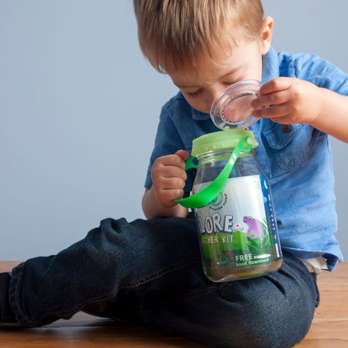 Young child examining a clear plastic bug catcher jar with a green glow-in-the-dark magnifying lid, promoting outdoor play and exploration in a handcrafted USA made toy from the Best Sellers collection.