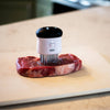 Compact white and black meat tenderizer with 58 stainless steel blades inserted into a raw steak on a cutting board, part of Kitchen & Food, Specialty Equipment, Butchering Supplies, and Best Sellers collections.