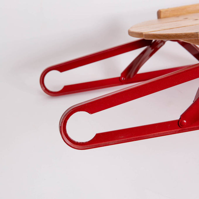 Close-up of vibrant red metal runners with circular cutouts beneath a smooth oak wood sled seat, showcasing handcrafted Amish made quality in children's outdoor play and USA Made collections.