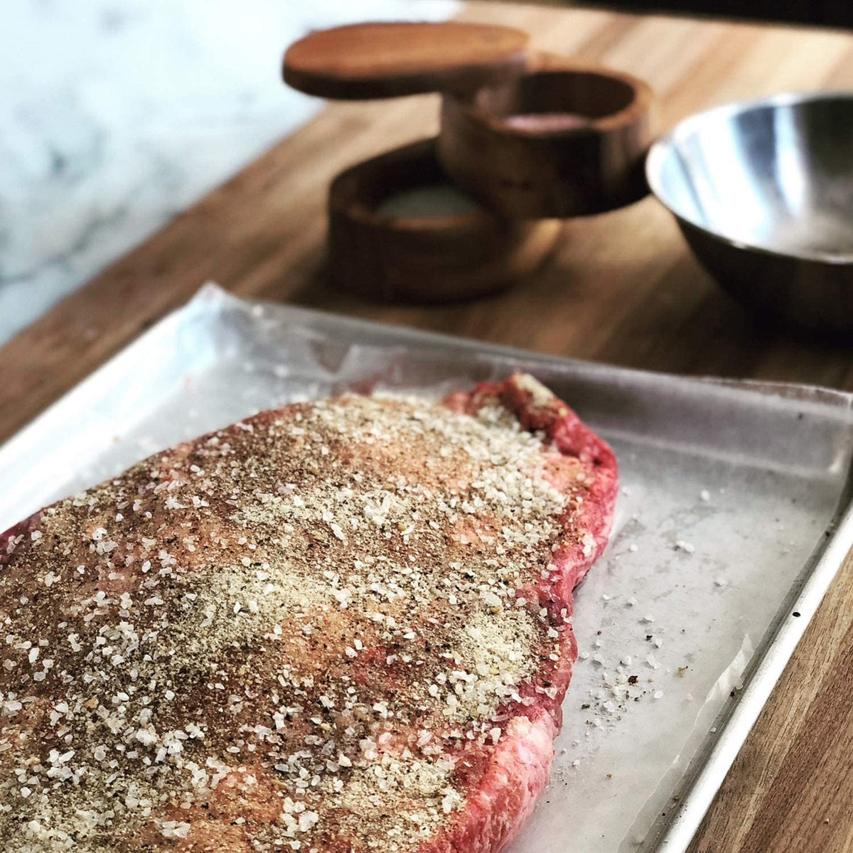 Handcrafted acacia wood salt cellar with a swivel lid, shown on a wooden countertop beside seasoned meat on a tray, ideal for Kitchen & Food, Storage and Serving, and Best Sellers collections.