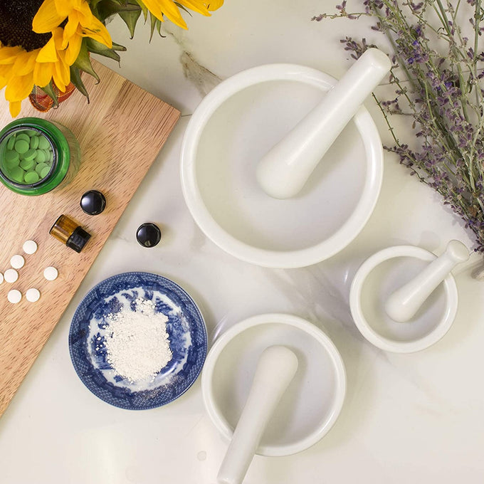 Set of three white porcelain mortar and pestles in small, medium, and large sizes, displayed with herbs, pills, and powder, ideal for Kitchen & Food, Food Prep, and Cooking Helpers collections.