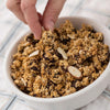 Handcrafted hearty granola clusters with almonds, walnuts, sunflower seeds, coconut, and raisins in a white bowl, made in USA for Kitchen & Food and Snacks collections.