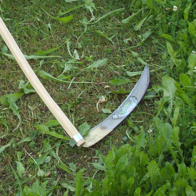 Close-up of a handcrafted wooden farming scythe with a curved metal blade resting on green grass, featured in Farm, Garden & Tool, Lawncare, Best Sellers, and Promo Eligible collections.
