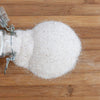 Glass jar spilling finely textured natural sea salt with visible trace minerals onto a wooden surface, suitable for Kitchen & Food, Pantry, USA Made, Best Sellers, and Promo Eligible collections.