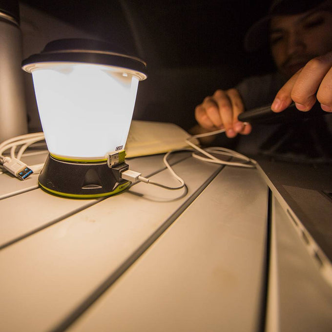 Bright rechargeable lantern emitting warm light on a table, with a USB cable connected to charge a device, featured in Lamps & Lighting and Emergency Supplies collections.
