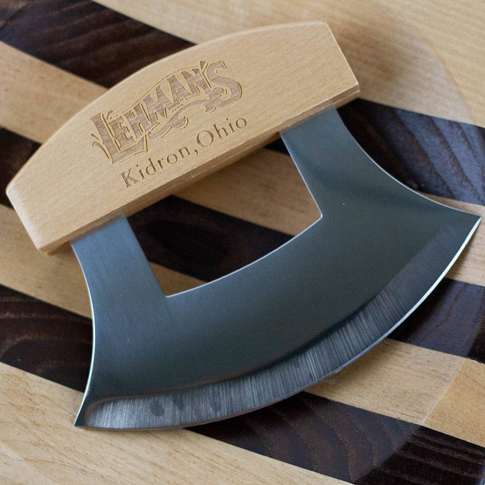 Crescent-shaped stainless steel ulu knife with a smooth wooden handle engraved with Lehman's Kidron Ohio, resting on a striped wooden cutting board, handcrafted and ideal for kitchen food prep and cutting collections.