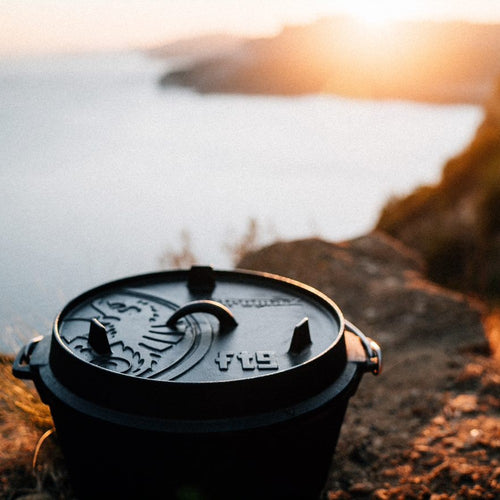 Cast iron Dutch oven with flat base and embossed lid featuring a dragon motif, resting on rocky terrain at sunset, ideal for Kitchen & Food, Cookware, Cast Iron, Best Sellers, Promo Eligible collections.
