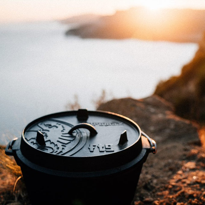 Cast iron Dutch oven with flat base and embossed lid featuring a dragon motif, resting on rocky terrain at sunset, ideal for Kitchen & Food, Cookware, Cast Iron, Best Sellers, Promo Eligible collections.