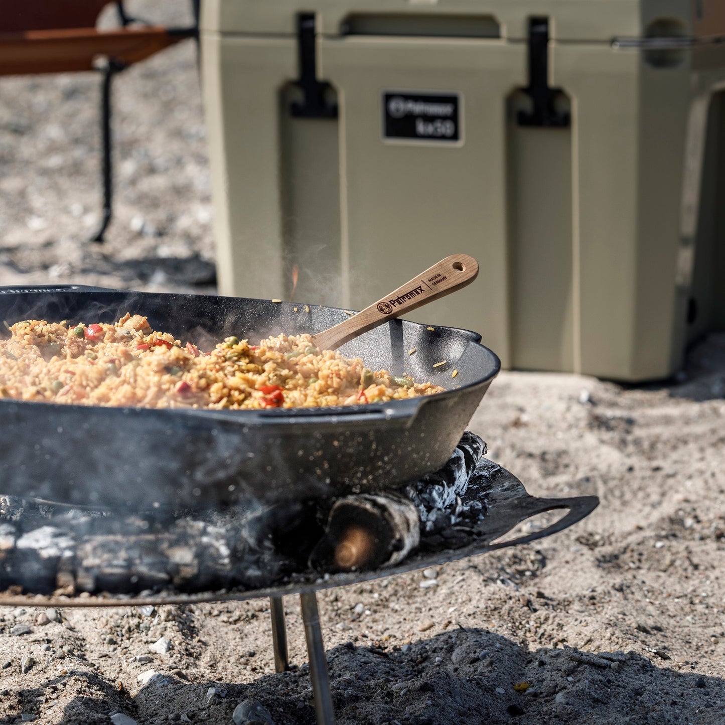 Rustic cast iron skillet with two handles cooking a mixed rice and vegetable dish over an open campfire, ideal for camping, kitchen, and farm use collections.