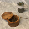 Handcrafted acacia wooden salt cellar with a swivel lid, filled with loose tea leaves, displayed on a marble countertop beside a ceramic mug and small silver spoon, ideal for Kitchen & Food and Storage and Serving collections.