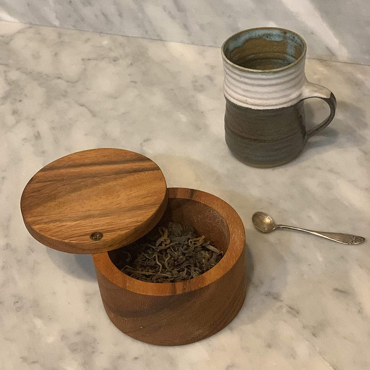 Handcrafted acacia wooden salt cellar with a swivel lid, filled with loose tea leaves, displayed on a marble countertop beside a ceramic mug and small silver spoon, ideal for Kitchen & Food and Storage and Serving collections.
