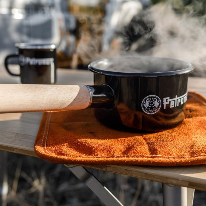 Black enamel pan with a wooden handle steaming on an orange mat atop a wooden table, designed for outdoor cooking in Camping, Farm, Garden & Tool, Cookware, Pots and Pans, Best Sellers, and Promo Eligible collections.