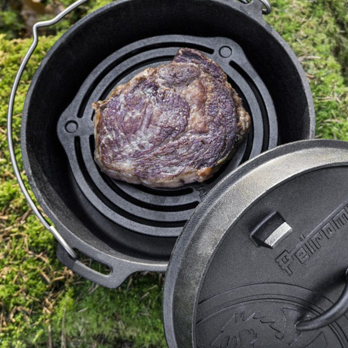 Cast iron stacking grate inside a Dutch oven with a seared steak cooking on top, ideal for even heat distribution during outdoor camping and kitchen use, featured in Farm, Garden & Tool, Kitchen & Food, Camping, Cookware, Cast Iron, Best Sellers, and Promo Eligible collections.