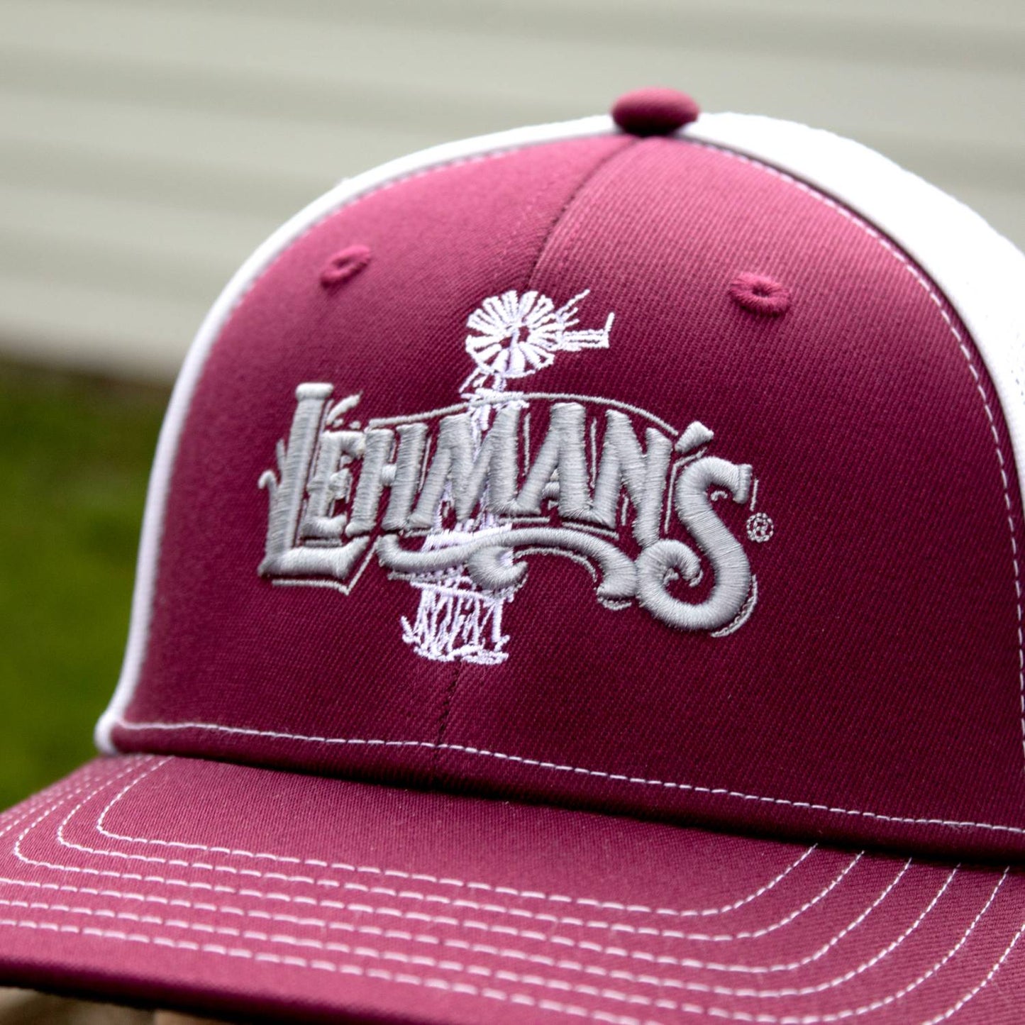Close-up of handcrafted trucker hat featuring embroidered white Lehman’s logo and windmill design on a burgundy front panel with white stitching, suitable for Health & Wellness, Clothing and Accessories, Best Sellers, and Promo Eligible collections.
