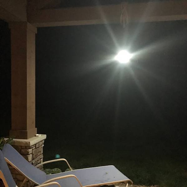 Bright outdoor rechargeable lantern hanging under porch roof, providing glowing light for nighttime camping, backyard, or emergency use, ideal for pest control and outdoor activities.